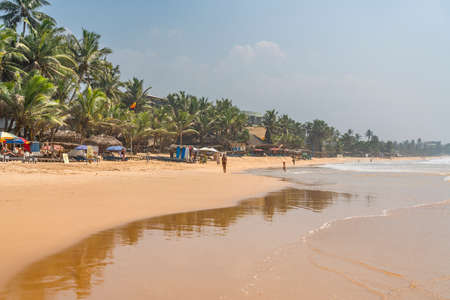 HIKKADUWA, SRI LANKA - JANUARY 22, 2022: Narigama beach at Hikkaduwa with people walking along the coastline with palmtreesのeditorial素材