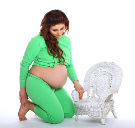 Pregnant woman kneeling next to a small white chairの写真素材
