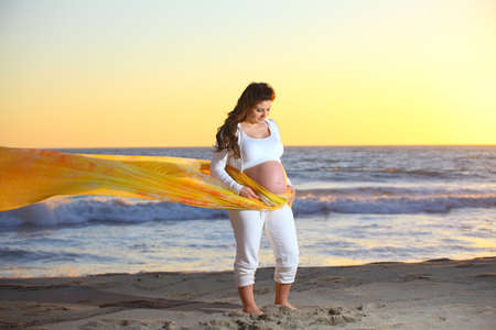 Pregnant woman holding her tummy at the beach during sunsetの写真素材
