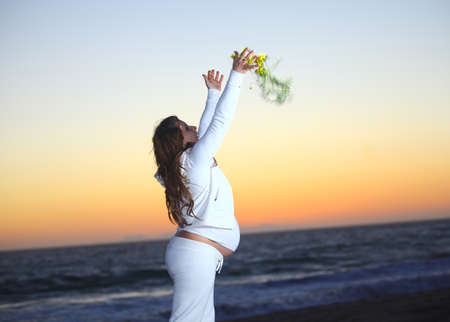 Pregnant woman at the beach during sunset tossing flowers in the air