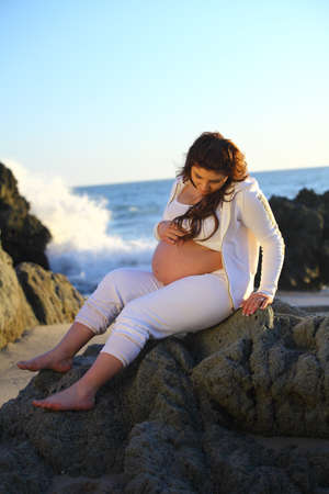 Pregnant woman sitting on the rocks at the beachの写真素材
