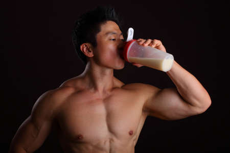 Asian Body Builder Drinking a Protein Shake on black backgroundの写真素材