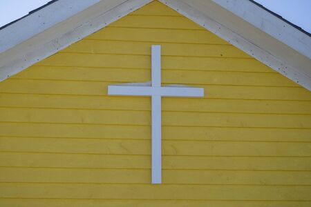 A cross on a yellow exterior wall with snow on top of the cross.の写真素材