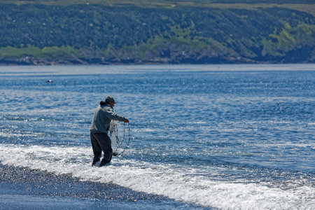 ST. VINCENTâS, NEWFOUNDLAND AND LABRADOR, CANADA - July 8, 2020.  A man using a casting net to catch caplin at the beach, taken on July 8, 2020, in St. Vincentâs.のeditorial素材