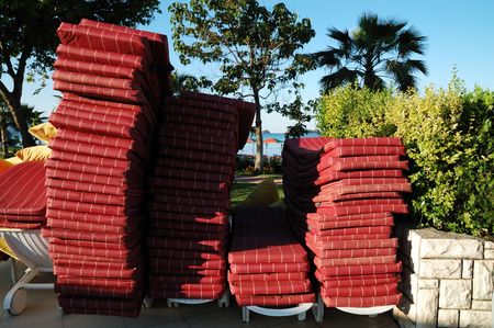 Stack of red sunbeds with plants and trees behindの写真素材