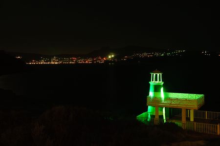 Lighthouse at night time against lights of a townの写真素材