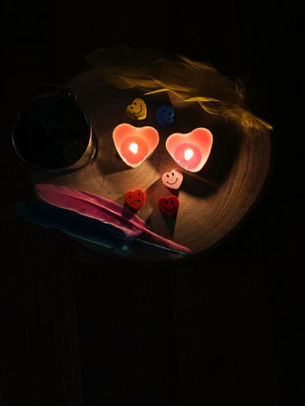 Heart-shaped candles on a wooden table in a dark room.の写真素材