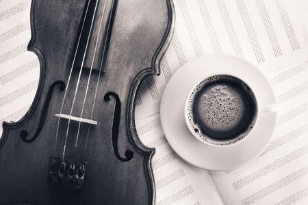 Violin acoustic classical stringed instrument and white coffee cup on sheet for musical notesの写真素材