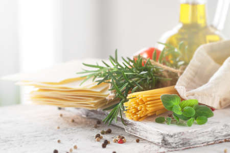 Healthy ingredients on a kitchen table - spaghetti, olive oil, tomatoes, spices and fresh italian herbs on a shiny background. Cooking or healthy life concept, horizontalの写真素材