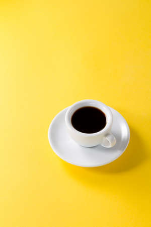 Coffee espresso in small white ceramic cup on yellow vibrant backgroundの写真素材