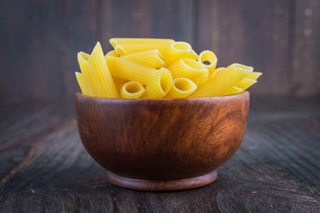 Raw pasta in wooden bowl on wood background - process old dark style picture