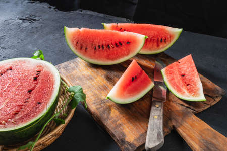 Watermelon slices cut in half on a wooden cutting board.の写真素材