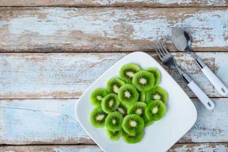 Fresh kiwi fruit in a plate on a wooden tableの写真素材
