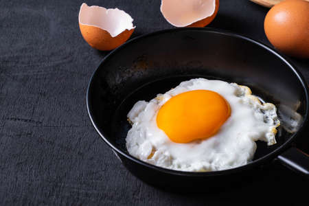 Fried eggs in a frying pan and egg shell for breakfast on a black background.