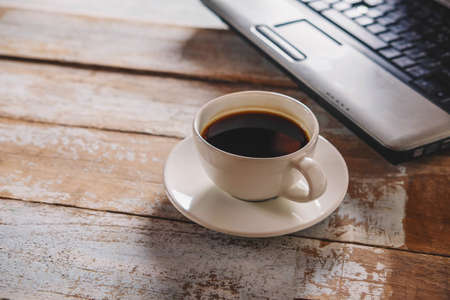 .A cup of coffee and a notebook computer on the deskの写真素材