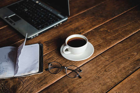 A coffee cup on the desk that has glasses and a notebook computerの写真素材