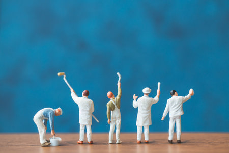Miniature people holding brush in front of a blue wall backgroundの写真素材