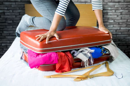Travel and vacation concept, happiness woman packing stuff and a lot of clothes into suitcase on bed prepare for her travel and journey tripの写真素材