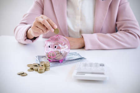 Business woman putting coins into piggy bank and using calculator to analysis business investment...