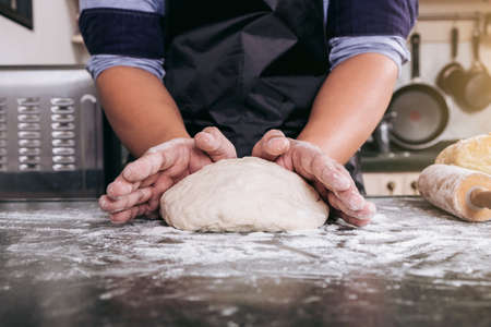 Male hands kneading dough sprinkled with flour table, Hands preparing bread, Raw dough for bread with ingredients on black backgroundの写真素材