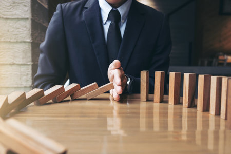 Close up of businessman hand Stopping Falling wooden Dominoes effect from continuous toppled or risk, strategy and successful intervention concept for businessの写真素材