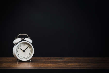 white alarm clock on wood table at night with dark or black background