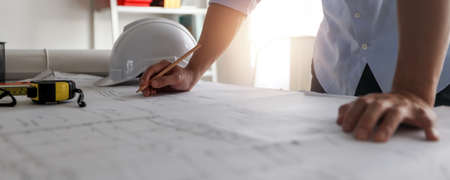Close up hand of engineer draw and draft on blueprint on table, architect working and creating in...