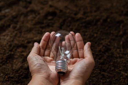 close up hand holding light bulb with soil, safe power and environment conceptの写真素材