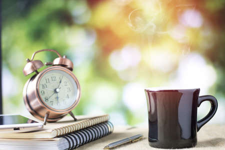 glass of coffee on table with book and clock in morning.の写真素材