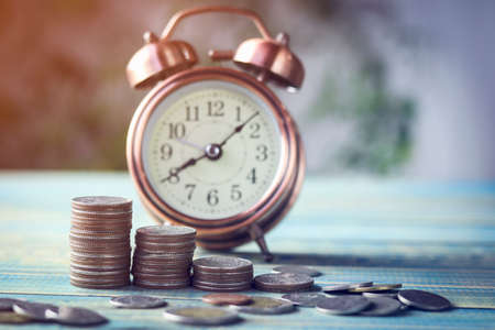 stacked of money with alarm clock on wood tableの写真素材