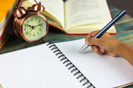 hand writing with books and clock on deskの写真素材