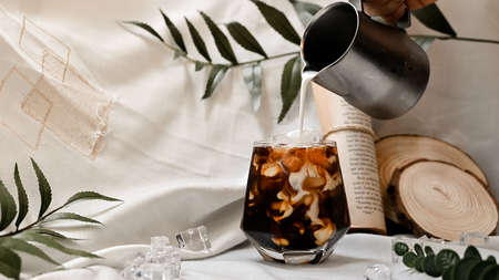 Barista pouring milk into a glass of iced coffee