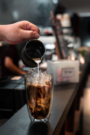 Barista pouring milk into a glass of iced coffee