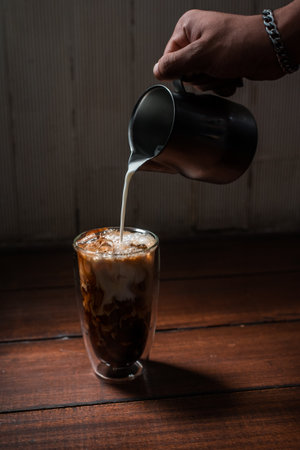 Barista pouring milk into a glass of iced coffeeの写真素材