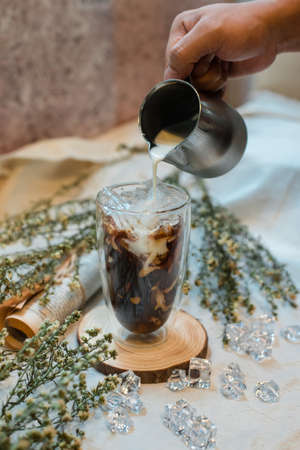 Barista pouring milk into a glass of iced coffee