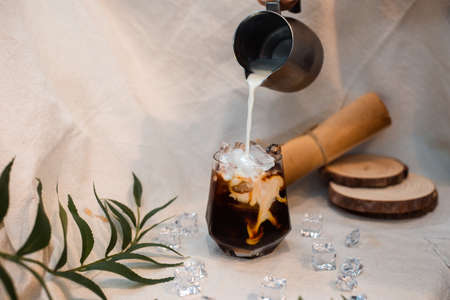Barista pouring milk into a glass of iced coffee