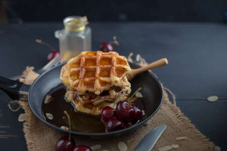 Honey on waffles with cherry berries on dark wooden background. breakfast concept
