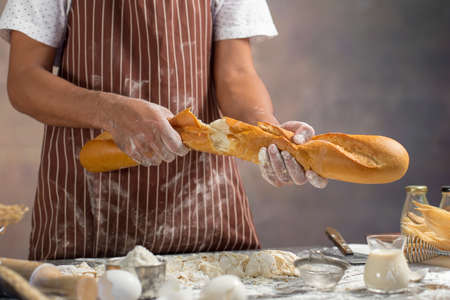 Chef holds the fresh bread in hand. Man preparing buns at table in kitchen