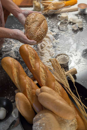 Chef holds the fresh bread in hand. Man preparing buns at table in kitchenの写真素材