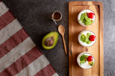 Glass of Cherry and avocado sliced in yogurt on wooden background