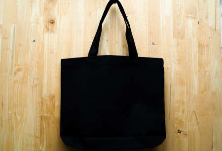 Black fabric bag on wooden background. Blank reusable bag. Flat lay