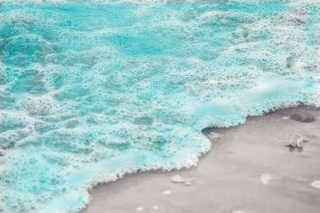 Close up blue sea water waves with white bubbles on sand beachの写真素材
