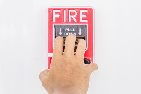 Hand of man pulling fire alarm switch on the white wall as background for emergency case at the new...