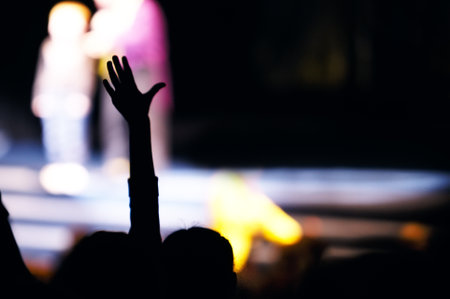 Supporter in the audience raising a hand at a live performance silhouetted against the blurred...