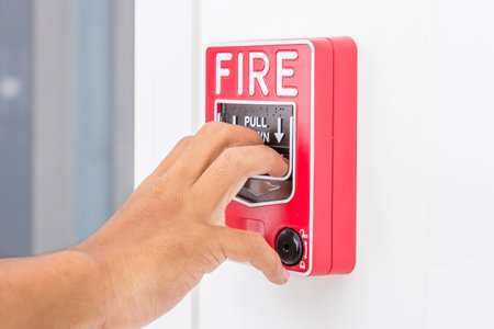 Hand of man pulling fire alarm switch on the white wall as background for emergency case at the new...