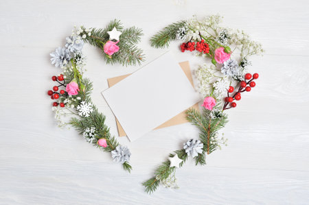 Mockup of Christmas Wreath in form of heart with sheet of paper Decorated with white snowflakes and cones. White wooden background with place for your text.の写真素材