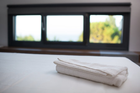 Close-up shot of a fresh white towel on the bed in hotel room, window with nature scene in backgroundの写真素材