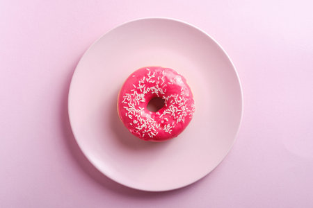 Pink red donut with white sprinkles on pink plate, sweet glazed dessert food on pink minimal background, top viewの写真素材