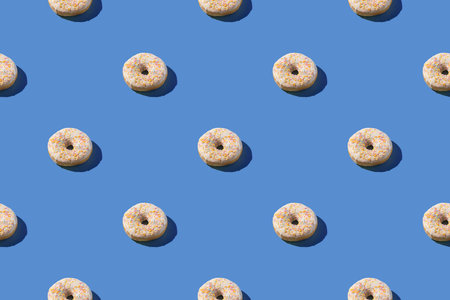Vanilla white donuts with sprinkles, sweet glazed dessert seamless pattern on blue backgroundの写真素材