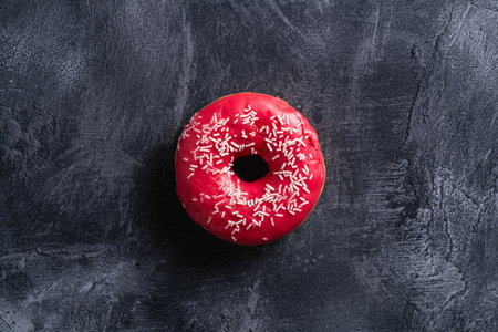 Pink donut with sprinkles, sweet glazed dessert food on dark concrete textured background, top viewの写真素材